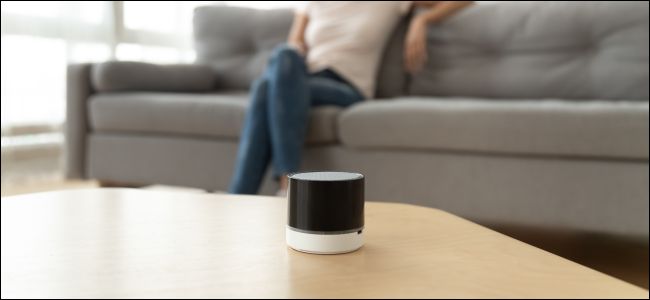 Speaker Bluetooth nirkabel di atas meja kopi di depan seorang wanita yang duduk di sofa.