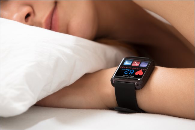 Seorang wanita tidur sambil menggunakan jam tangan pintar menunjukkan detak jantungnya.