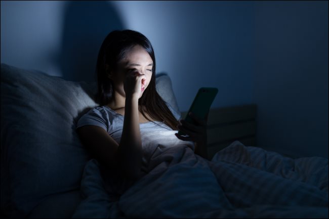 Seorang wanita menggunakan smartphone di tempat tidur pada malam hari.