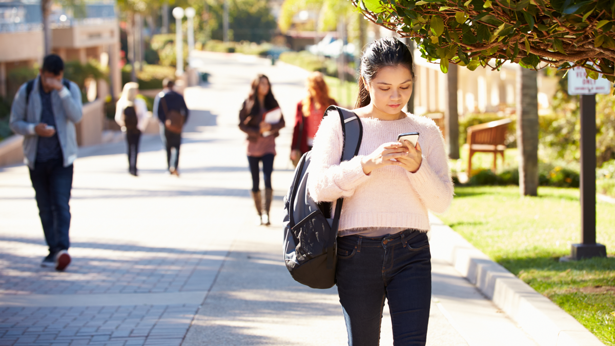 Sinh viên vừa đi dạo ngoài trời trong khuôn viên trường đại học vừa sử dụng điện thoại