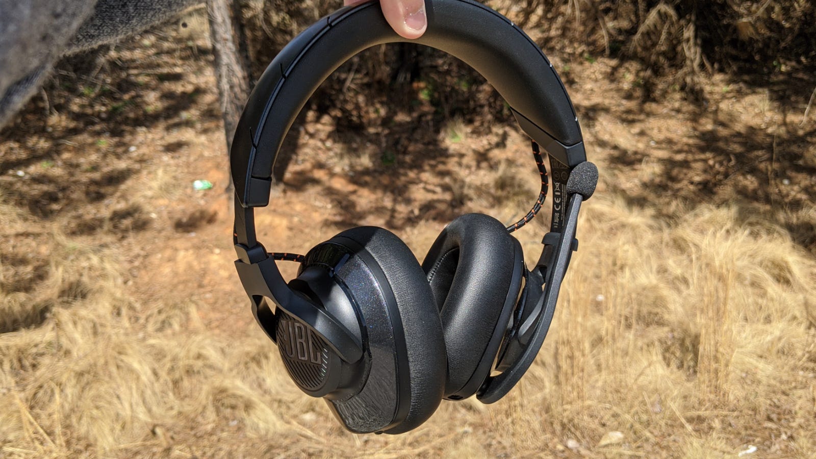 Headphone JBL Quantum 600 dipegang di lantai hutan