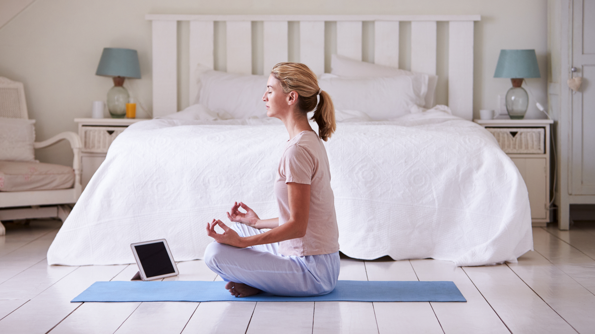 Wanita dengan tablet digital menggunakan aplikasi meditasi di kamar tidur