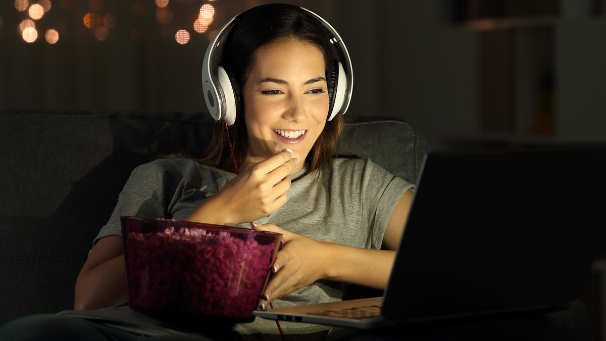Seorang gadis makan popcorn sambil mengobrol video dan menonton Netflix bersama teman-temannya.