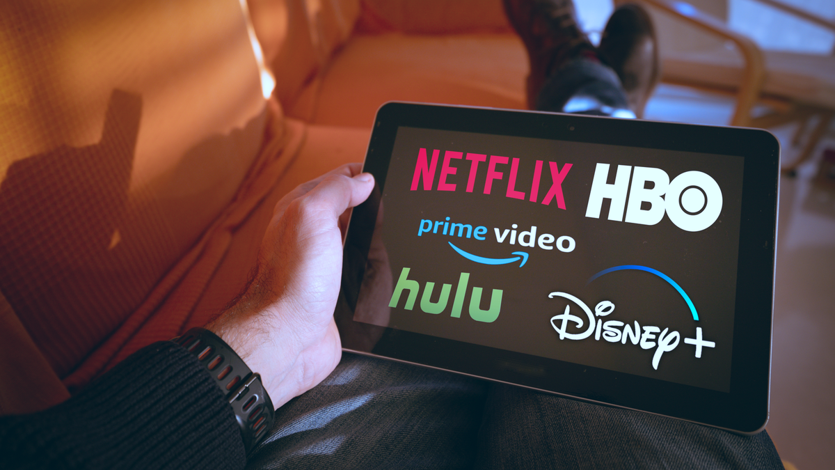 Pria memegang tablet dengan Netflix, Hulu, Amazon Logo video, HBO dan Disney+ 