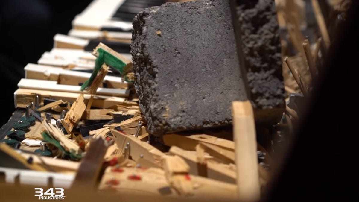Keyboard piano rusak, dengan batu raksasa bertumpu pada tuts yang hancur.