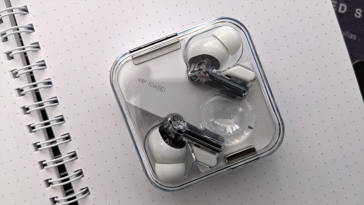 Foto headphone Nothing Ear 1 di selembar kertas putih. Artikel itu menunjukkan melalui Telinga 1 dari kasing transparan.