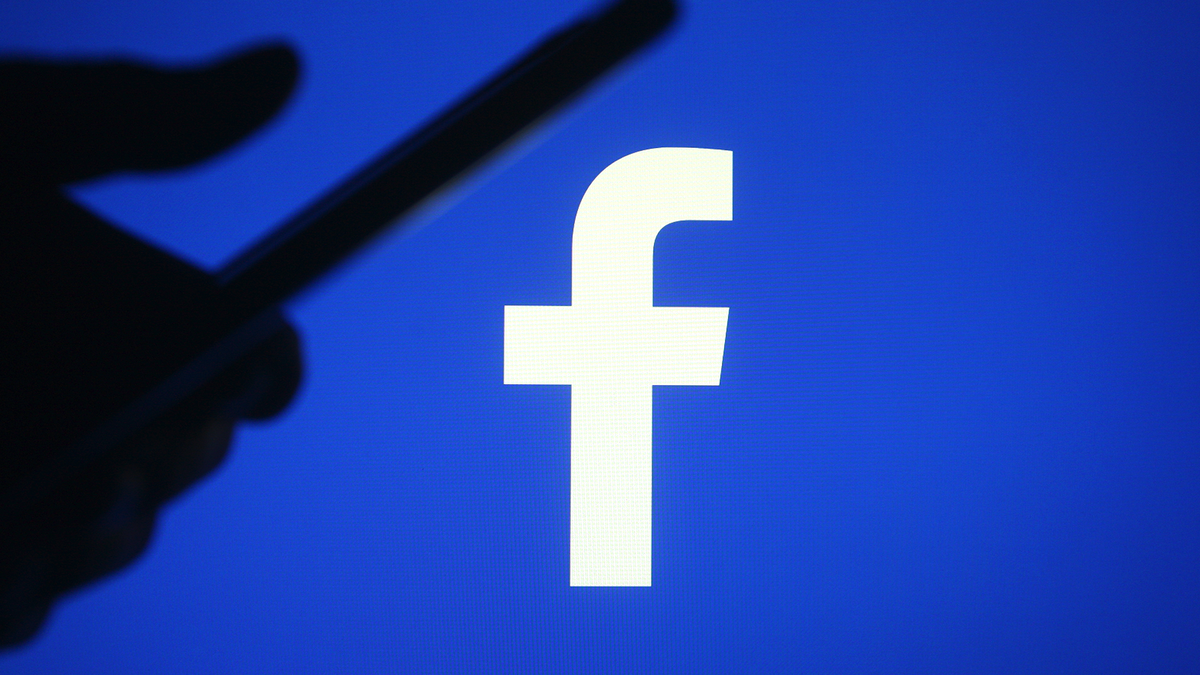 Các Facebook biểu tượng với một bàn tay silohette bằng cách sử dụng điện thoại thông minh.
